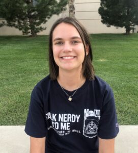 woman sitting outisde with short brown hair and a "talk nerdy to me" shirt on