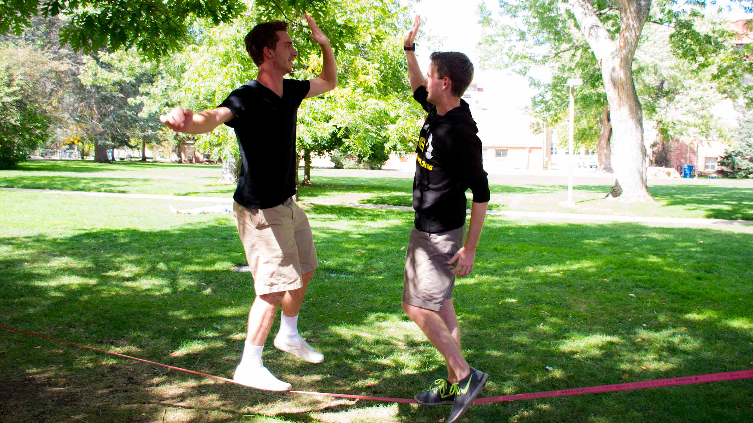 Two students high-fiving on a slack line